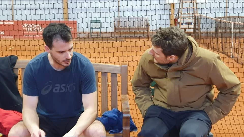 Deux hommes échangent au bord d’un court couvert